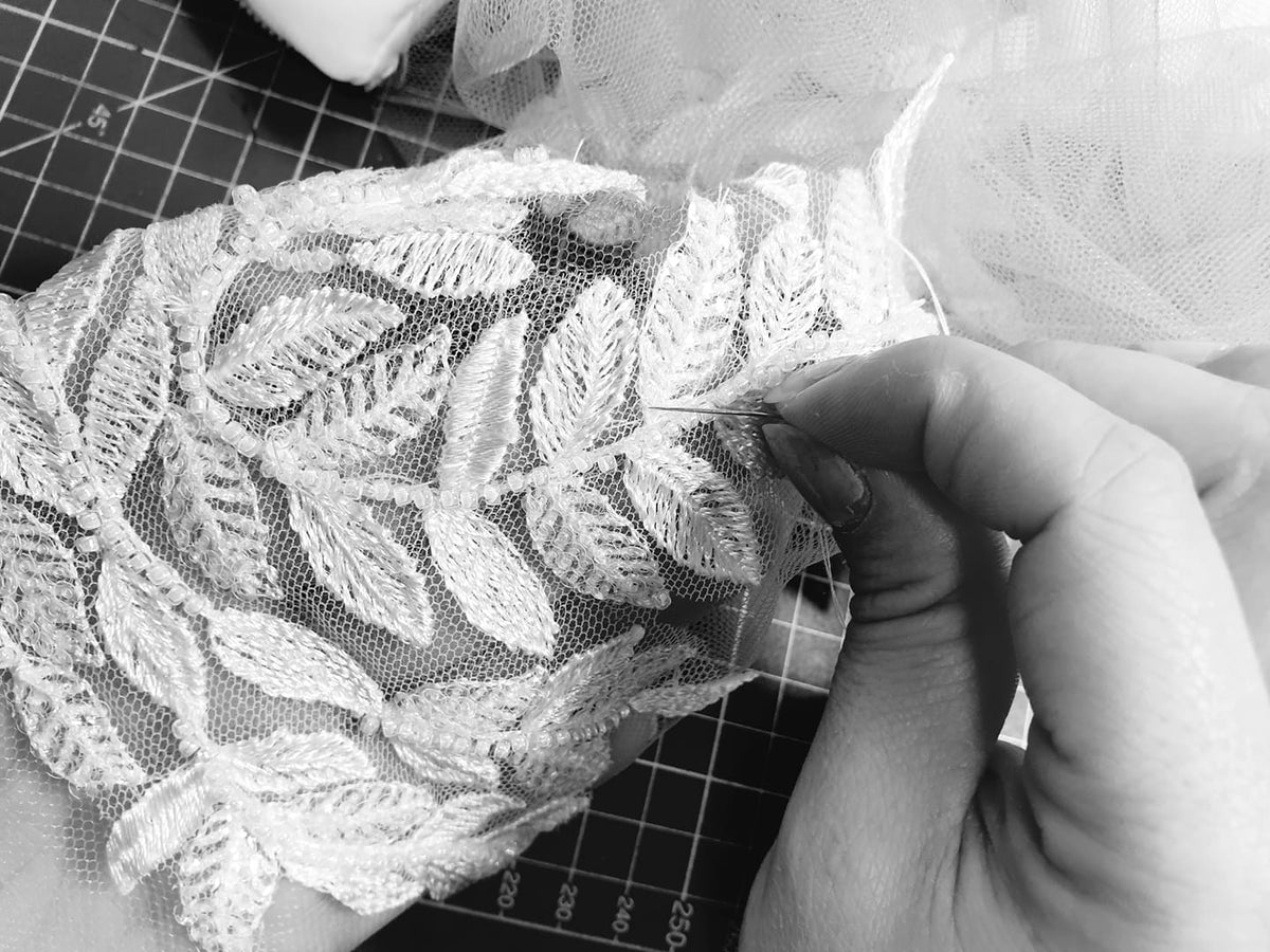 Les mains de l'atelier posent un motif de dentelle sur une manche en tulle